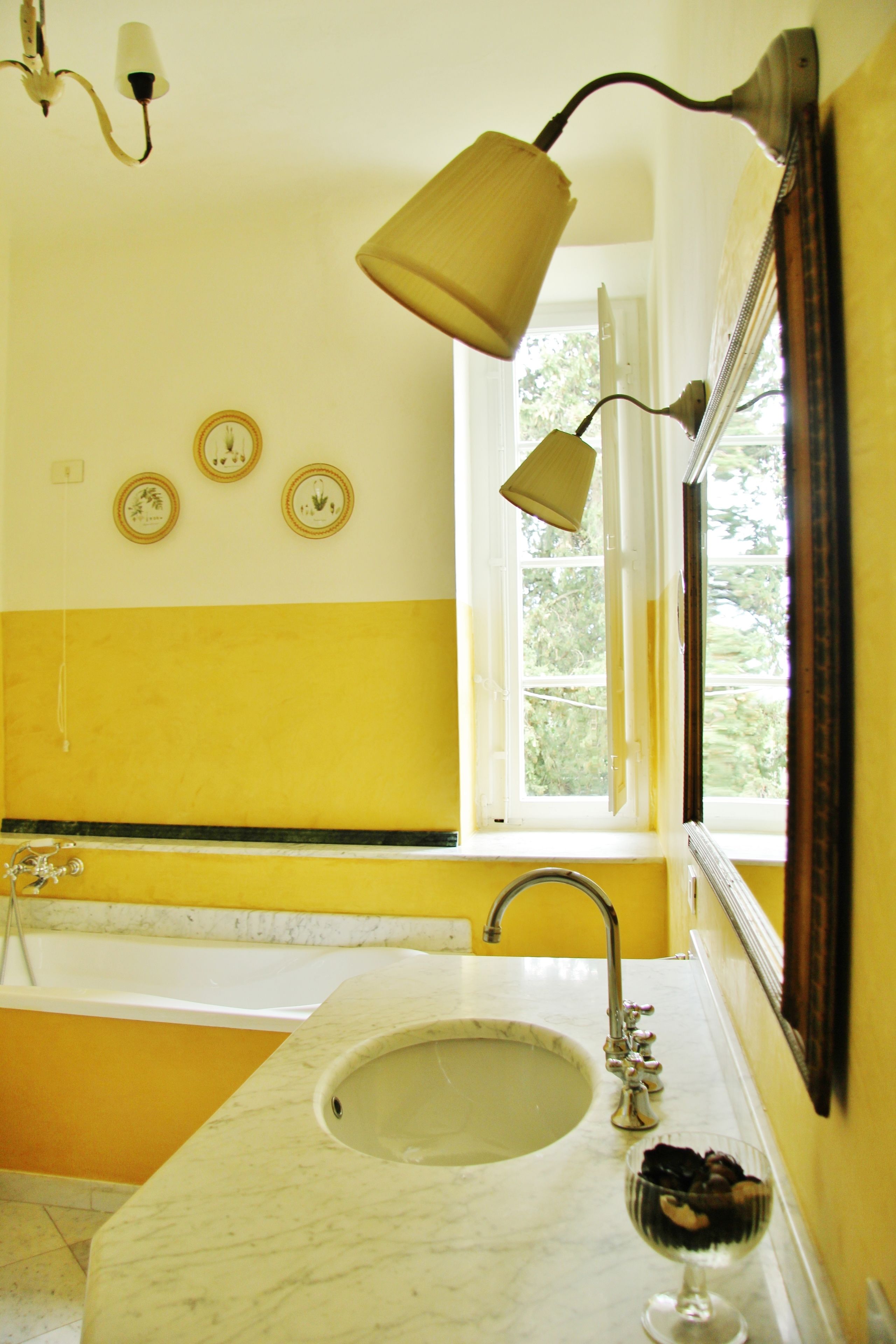Une salle de bain aux couleurs jaune et blanc, avec un lavabo, un miroir et une fenêtre.