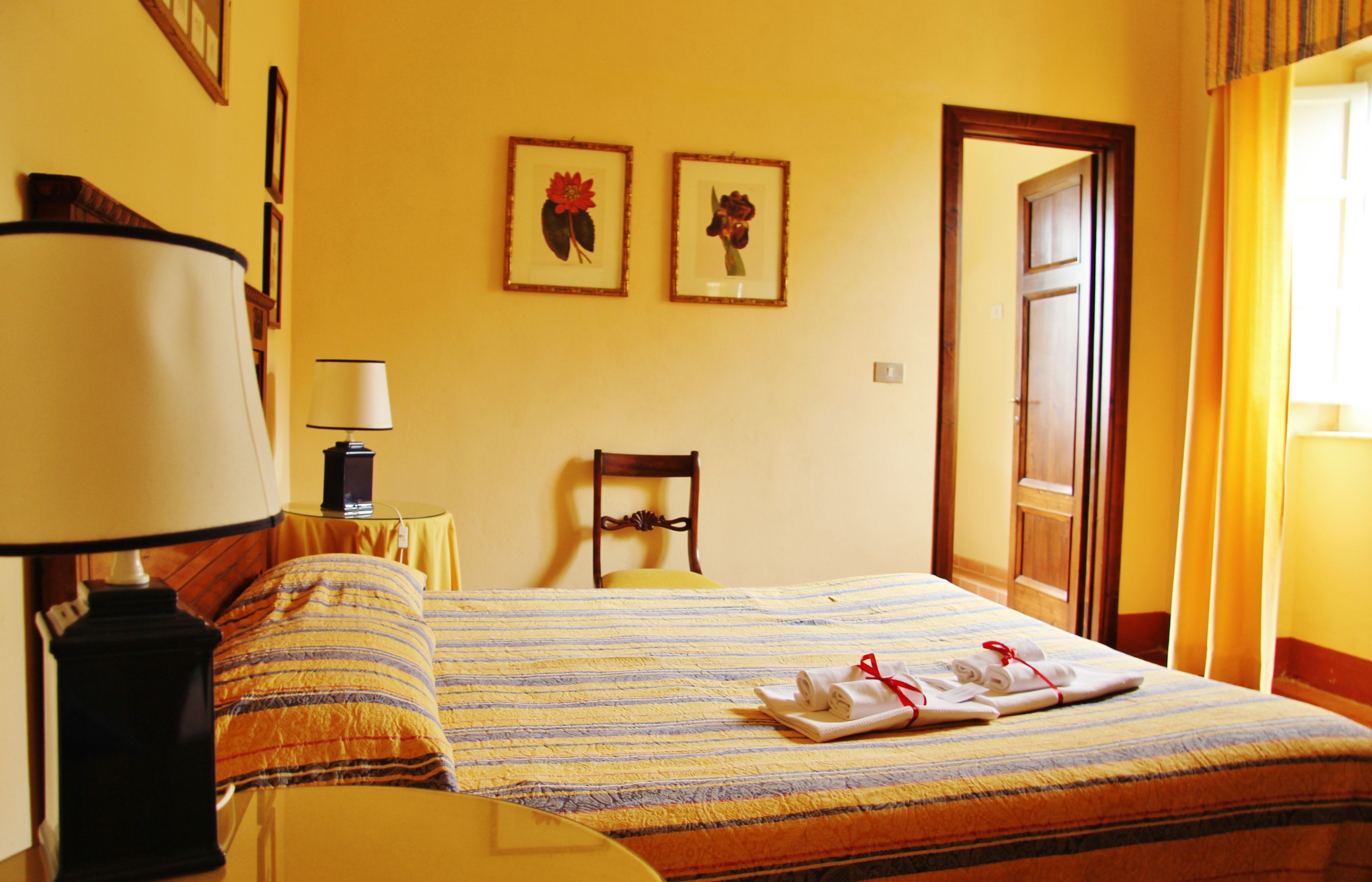 Une chambre d’hôtel avec un lit, une chaise, une lampe et deux tableaux encadrés au mur.
