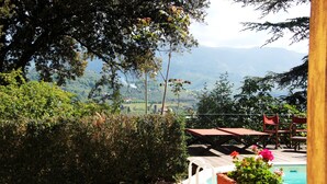 A poolside area with a view of mountains, a wooden deck, and a seating area with chairs and a table. - Agriturismo Villa Pedone (Lucca)