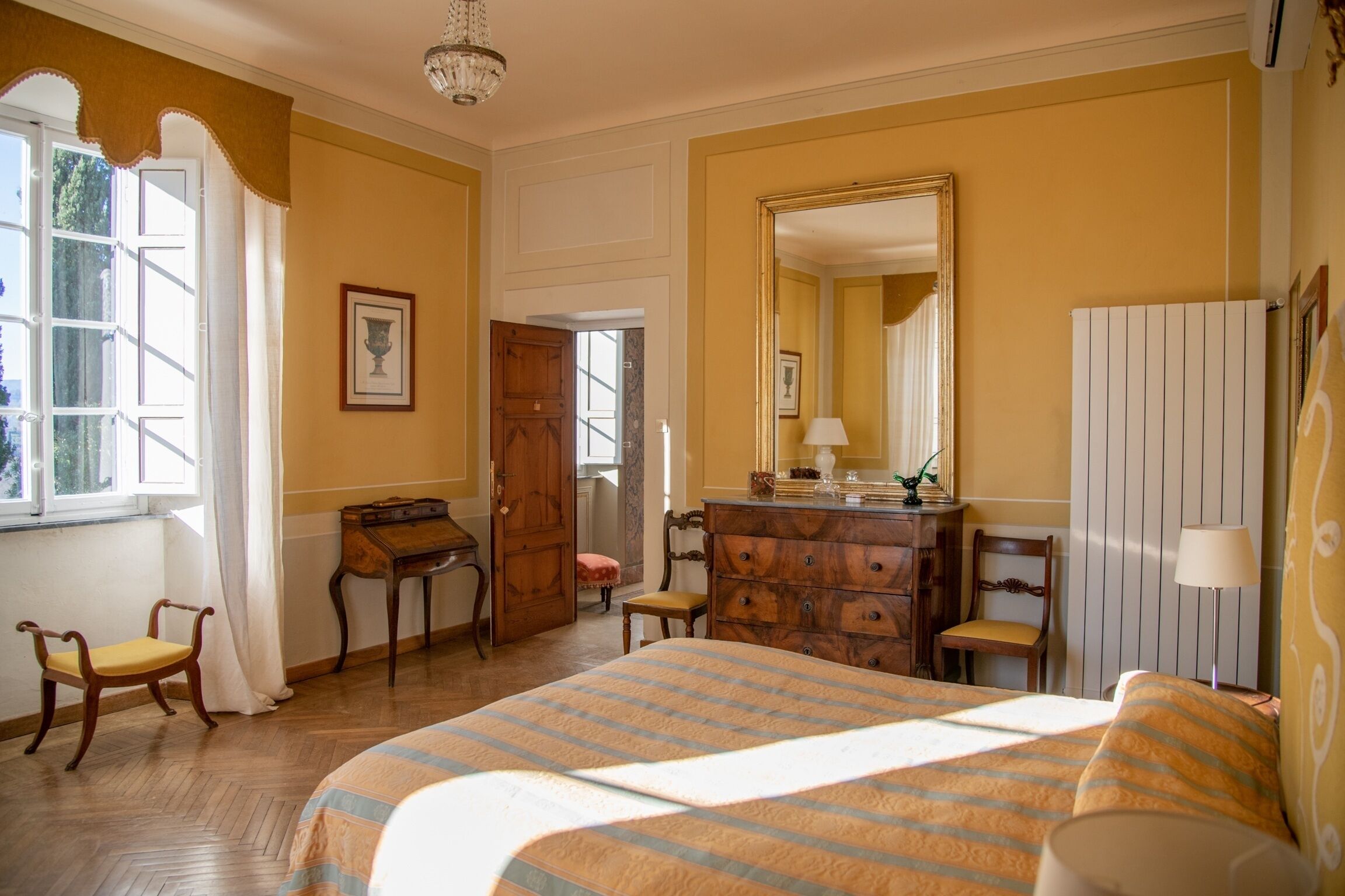Une pièce comprenant un lit, une commode en bois, un bureau, des chaises et un grand miroir.