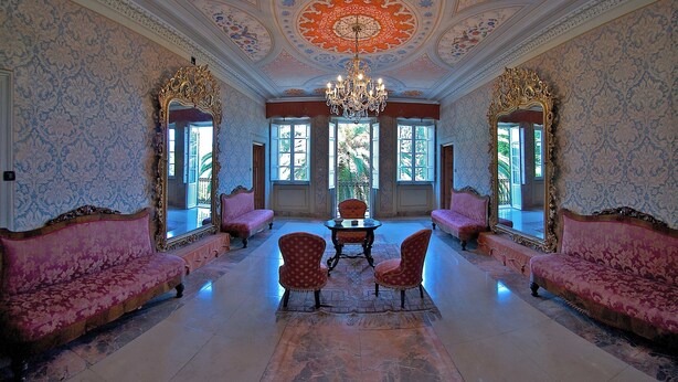 A grand room with ornate wallpaper, a chandelier, and two sofas facing a table. - Agriturismo Villa Pedone (Lucca)