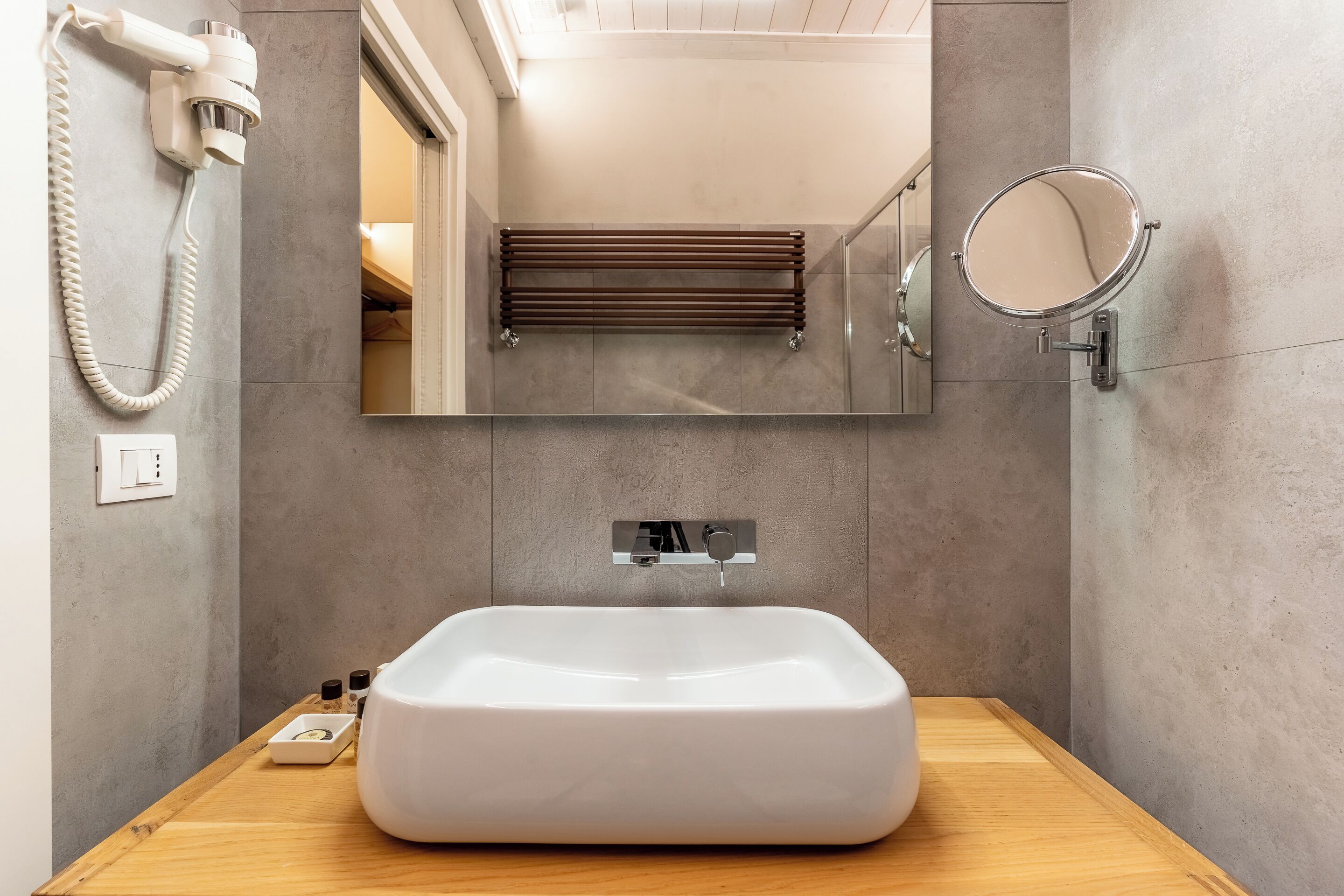 A bathroom with a large rectangular sink, a handheld hair dryer, a towel rack, and a mirror.