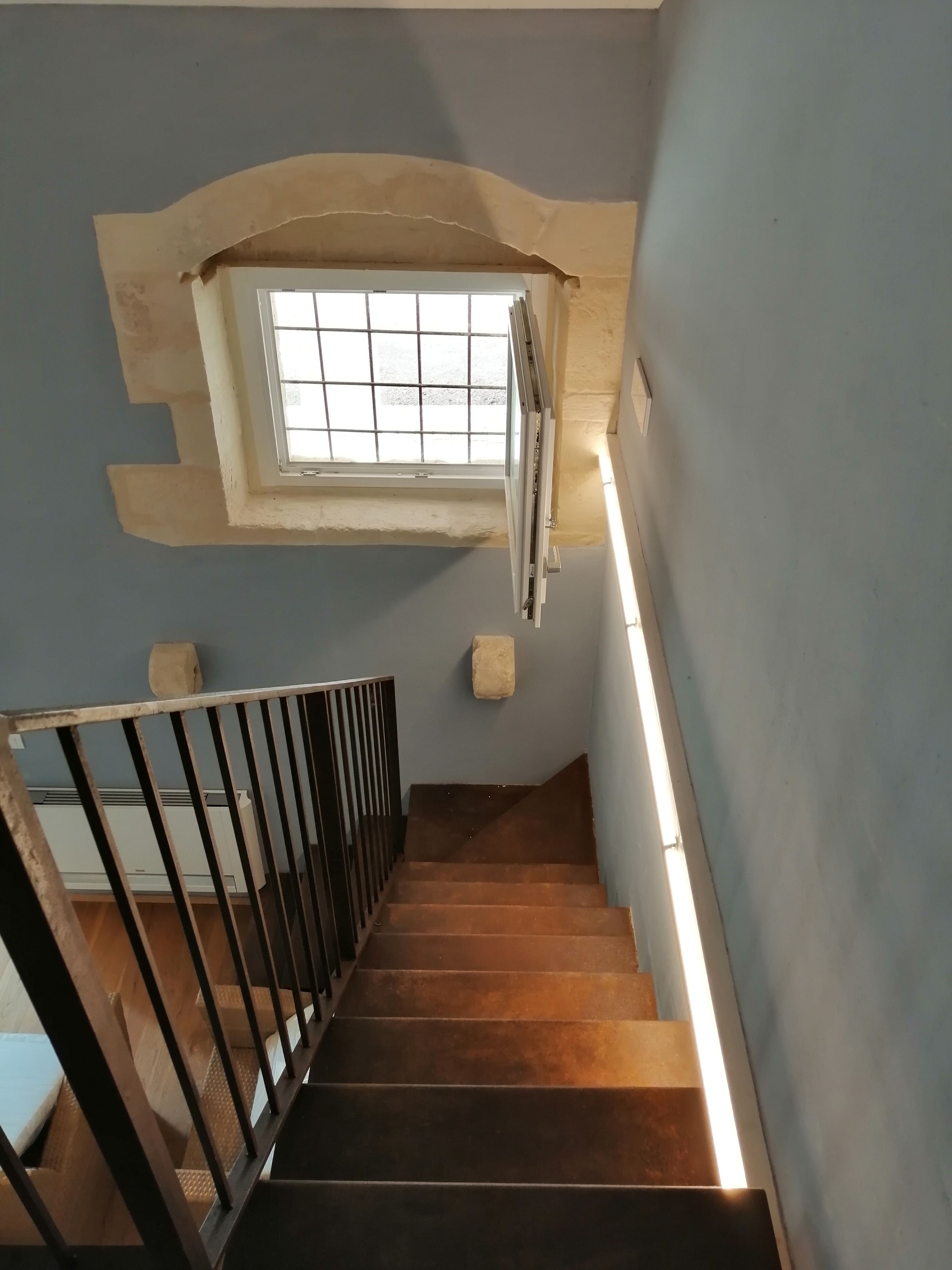 Una escalera con una ventana en la parte superior, barandilla y un radiador fijado a la pared.