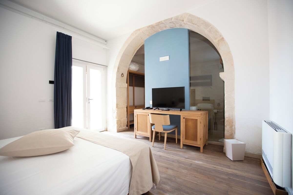 A hotel room with a bed, a desk, a chair, and a television.