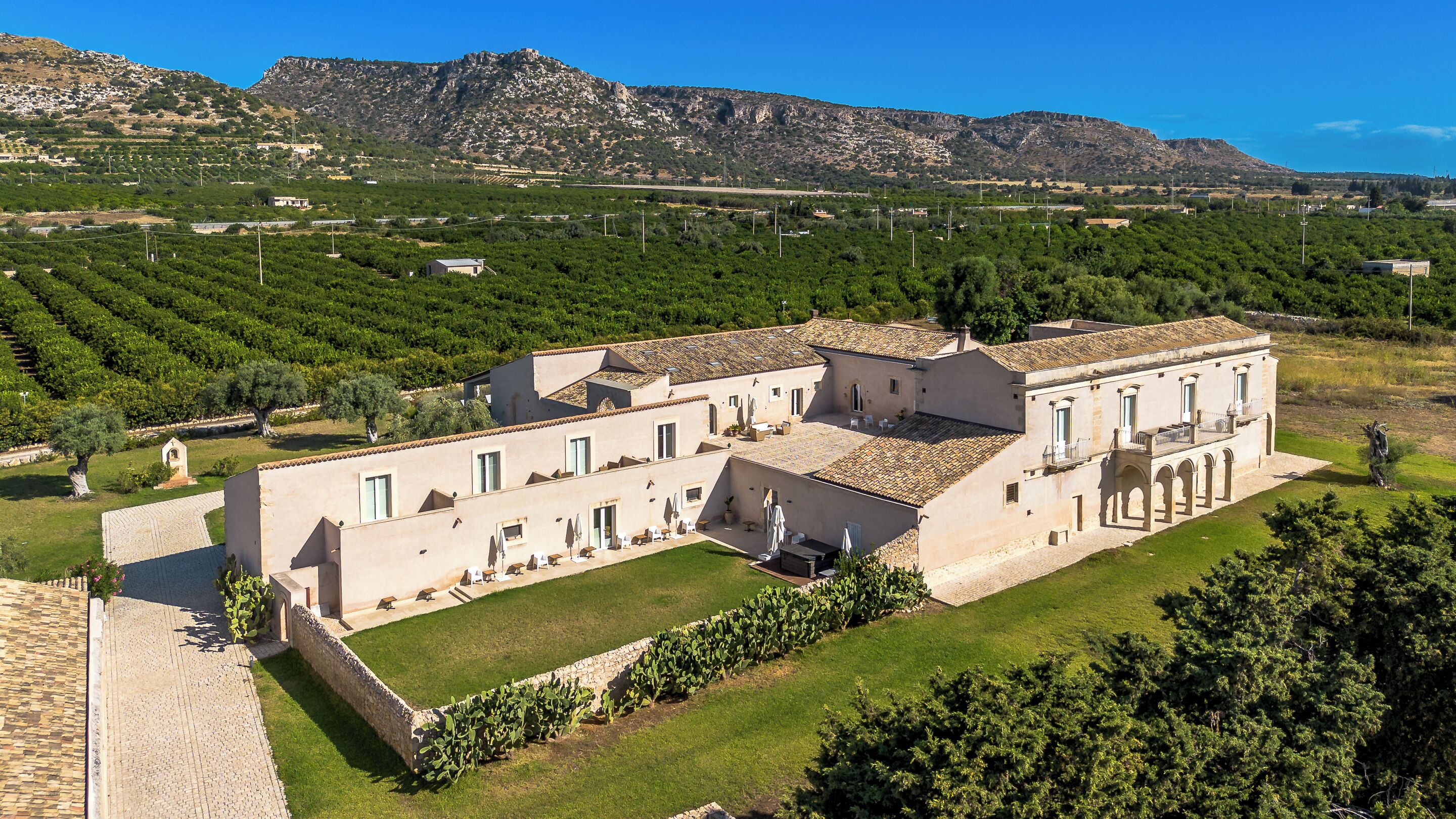 A large, historic building with multiple rooms and a courtyard, surrounded by lush greenery and vineyards.