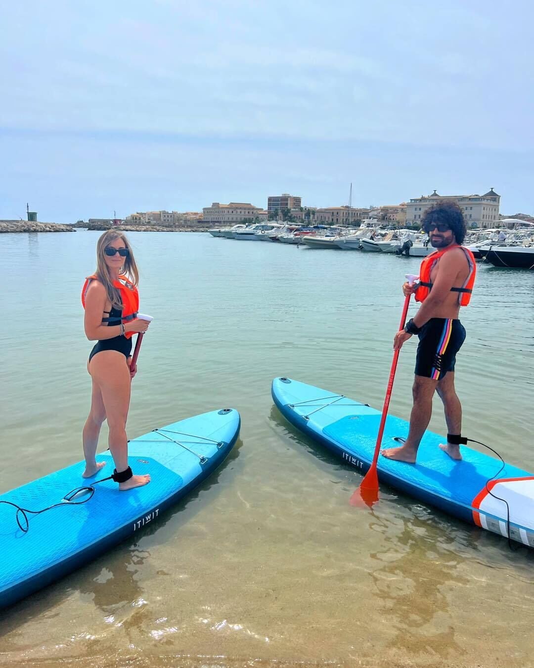Two paddleboards on a calm body of water with buildings in the background.