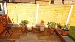 Un patio con suelo de piedra, un banco de madera y plantas en macetas.