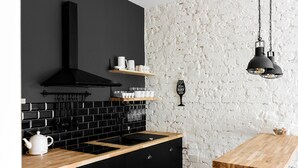 A kitchen with black cabinets, a wooden countertop, a black range hood, and hanging utensils. - Urban Rustic Flat in Historical  Building (Śródmieście)