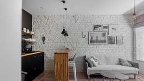 A modern living room with a white brick wall, a wooden coffee table, a grey sofa, and a black cabinet. - Urban Rustic Flat in Historical  Building (Śródmieście)