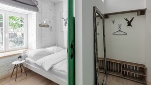A bedroom with a bed, a window, a small table, and a mirror. - Urban Rustic Flat in Historical  Building (Śródmieście)