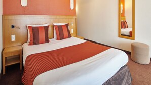 Une chambre d’hôtel comprenant un lit, des tables de chevet, une petite table, un miroir et un luminaire fixé au mur.