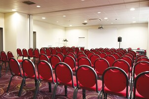 A conference room with rows of red chairs, a projector screen, and a whiteboard.