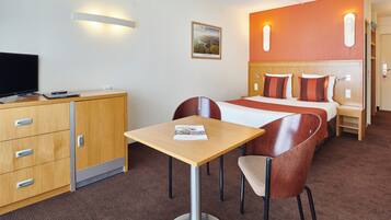 Une chambre d’hôtel comprenant un lit, une table de chevet, un bureau avec une chaise, une télévision et une armoire.