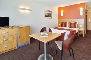 Ett hotellrum med en säng, ett nattduksbord, ett skrivbord med en stol, en tv och en garderob.