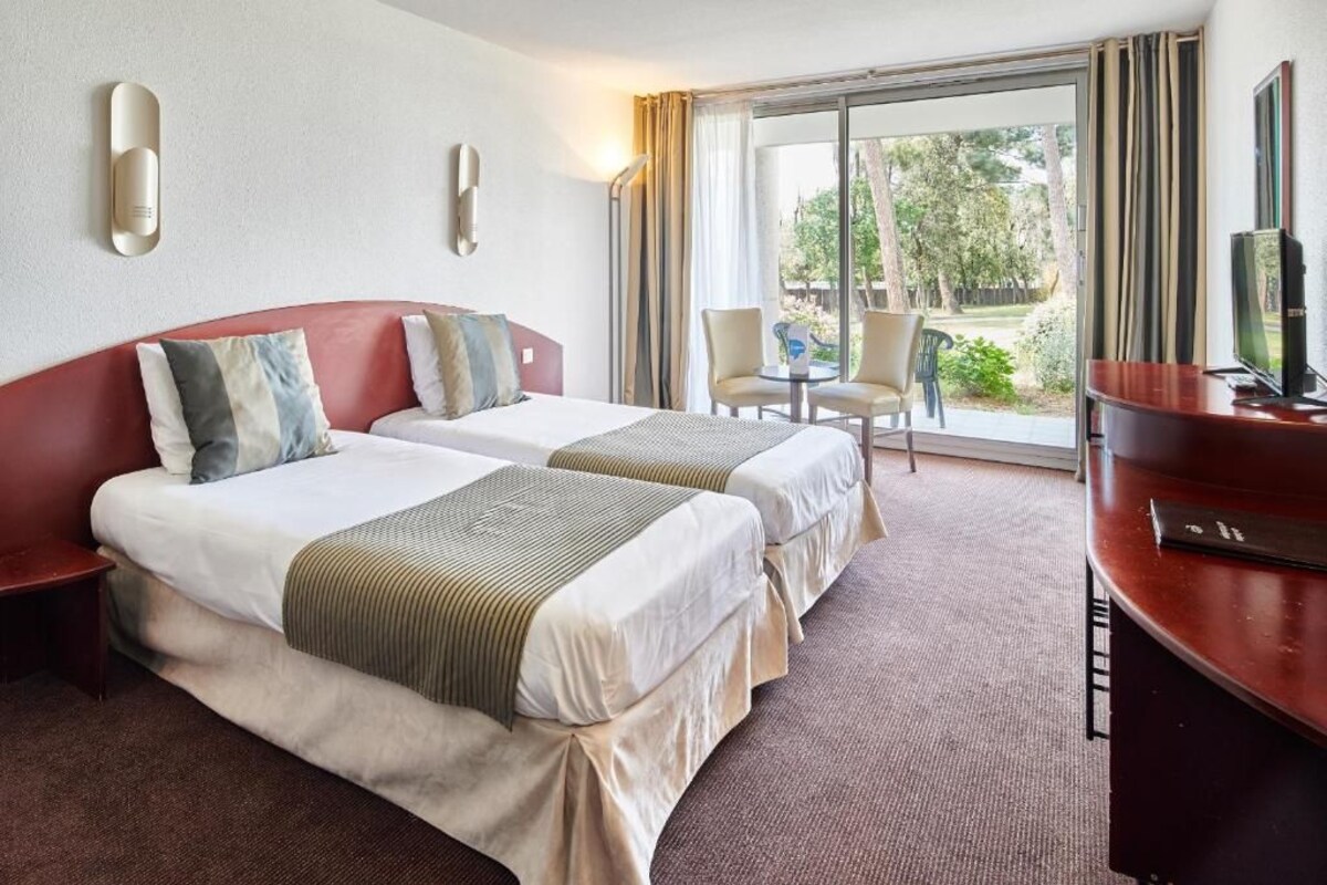 Quarto de hotel com duas camas, uma escrivaninha, televisão e porta de vidro deslizante para o exterior.