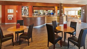 Un hall d’hôtel avec des tables et des chaises rondes, un comptoir d’accueil et un espace bar.