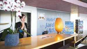 Un comptoir d’accueil d’hôtel agrémenté d’un vase de fleurs d’orchidées blanches, d’une lampe et d’un présentoir à brochures.