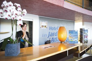 Mostrador de recepción de hotel con un jarrón de orquídeas blancas, una lámpara y un expositor de folletos.