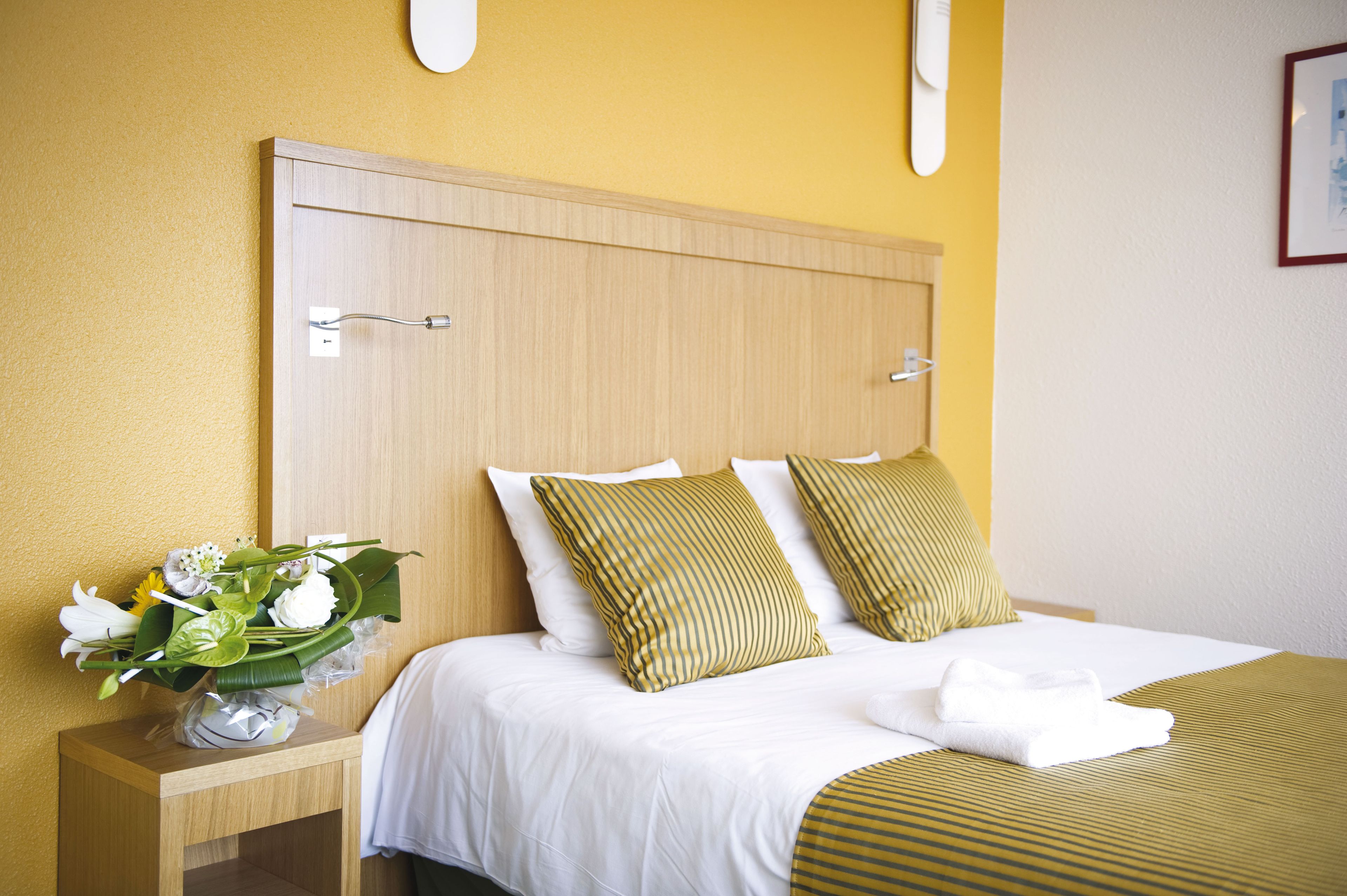 A hotel room with a wooden headboard, white bedding, and a bedside table with a vase of flowers.