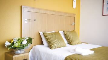 A hotel room with a wooden headboard, white bedding, and a bedside table with a vase of flowers.