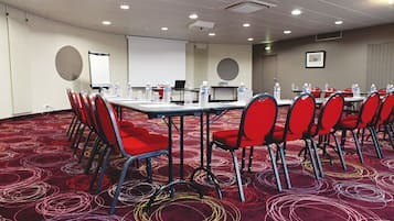 A conference room with a carpeted floor, red chairs, a table with water bottles, a projector screen, and a laptop.
