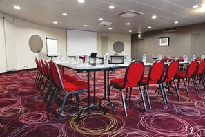 A conference room with a carpeted floor, red chairs, a table with water bottles, a projector screen, and a laptop. - Club Les Jardins De L'atlantique (Talmont-Saint-Hilaire)