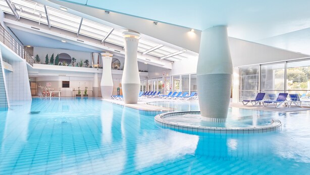 Une piscine intérieure dotée de plusieurs couloirs de nage, de chaises longues et d’un espace baigné de lumière naturelle grâce à de grandes fenêtres.