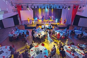 A banquet hall with round tables set for dining, a stage with performers, and a large audience seated. - Club Les Jardins De L'atlantique (Talmont-Saint-Hilaire)