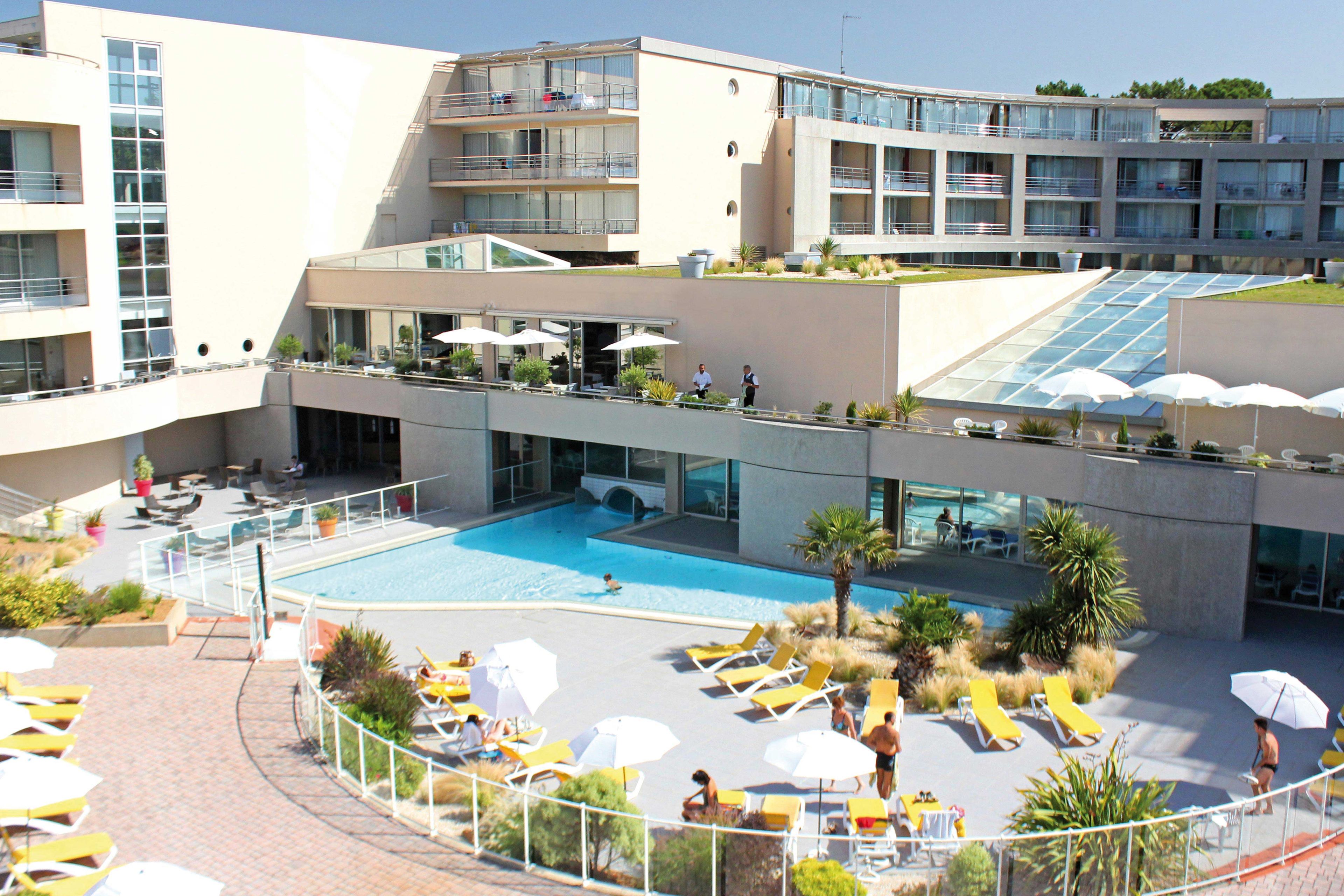A modern hotel with a rooftop pool, multiple balconies, and outdoor seating areas.
