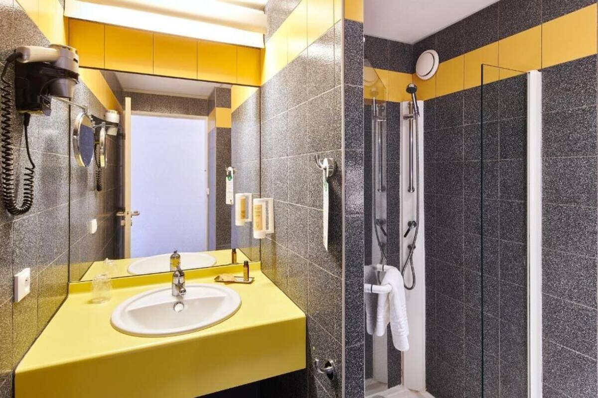 A bathroom with a yellow sink, a mirror, a hairdryer, and a shower with a glass door.