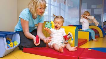 A child playing with toys on a colorful play mat in a room with a window in the background.