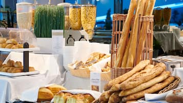 A buffet with various breads and pastries, including baguettes and croissants, displayed in baskets and on trays.