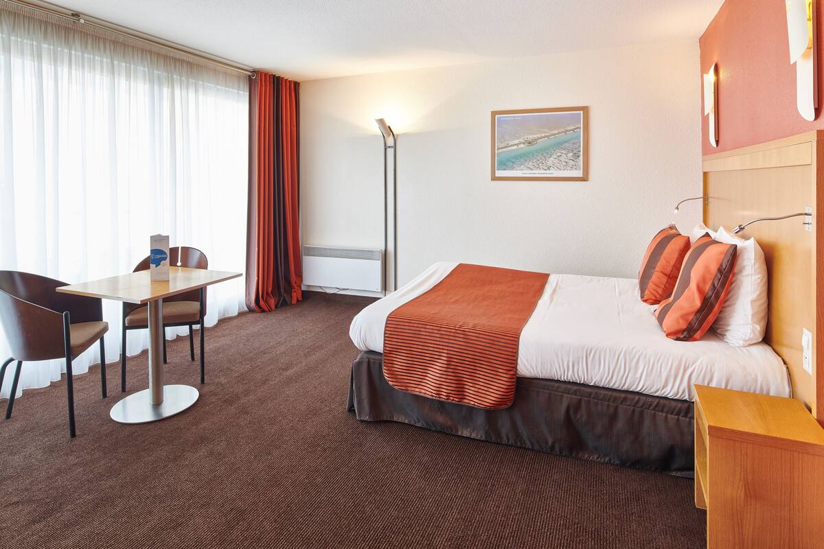 A hotel room with a bed, a desk, and a chair.