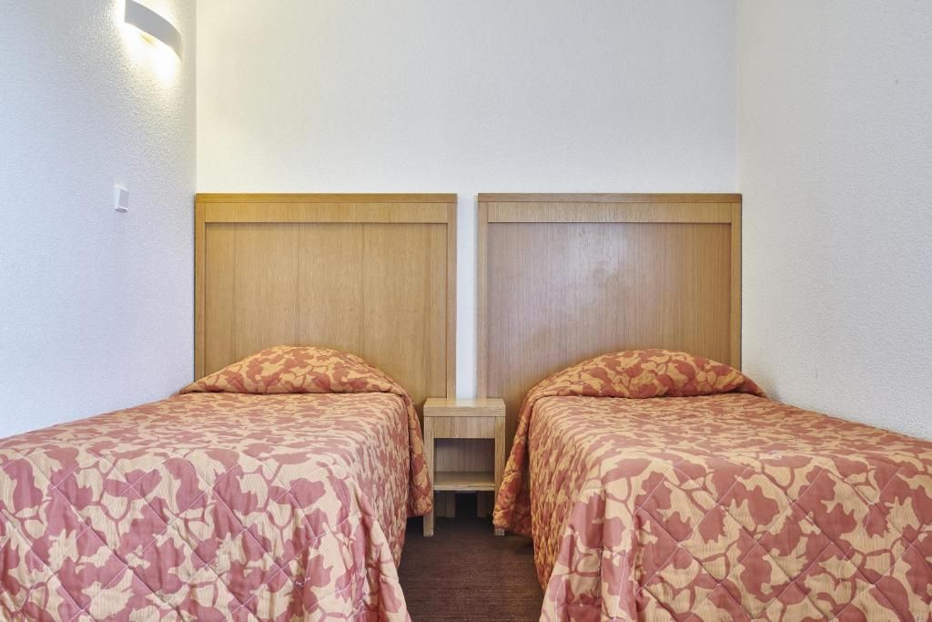 A room with two single beds, wooden headboards, a small bedside table, and a carpeted floor.