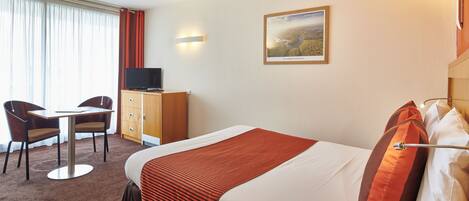 A hotel room with a bed, a desk, a chair, a television, and a painting on the wall.