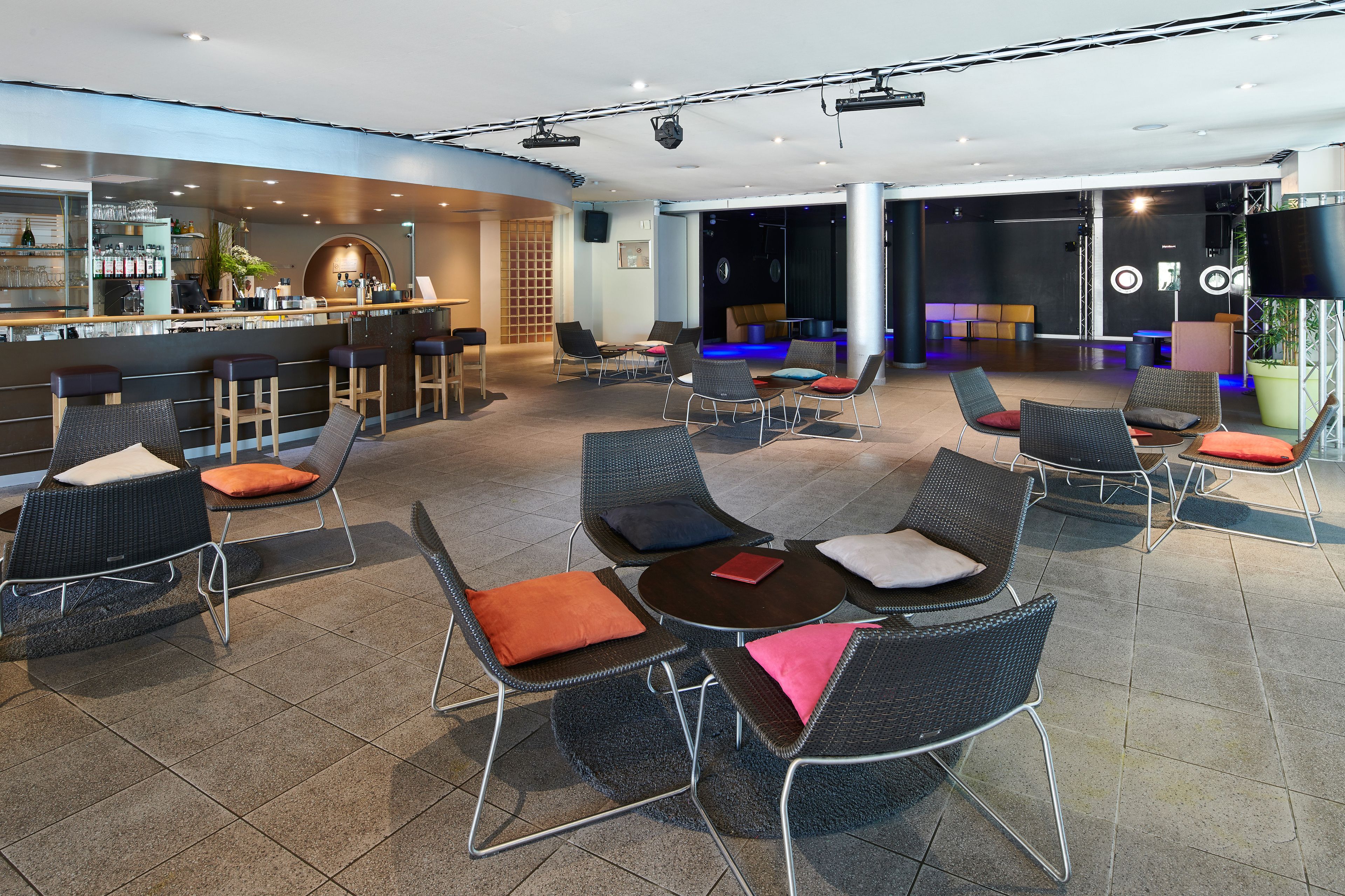 A modern lounge area with seating arrangements, a bar, and a stage for presentations.