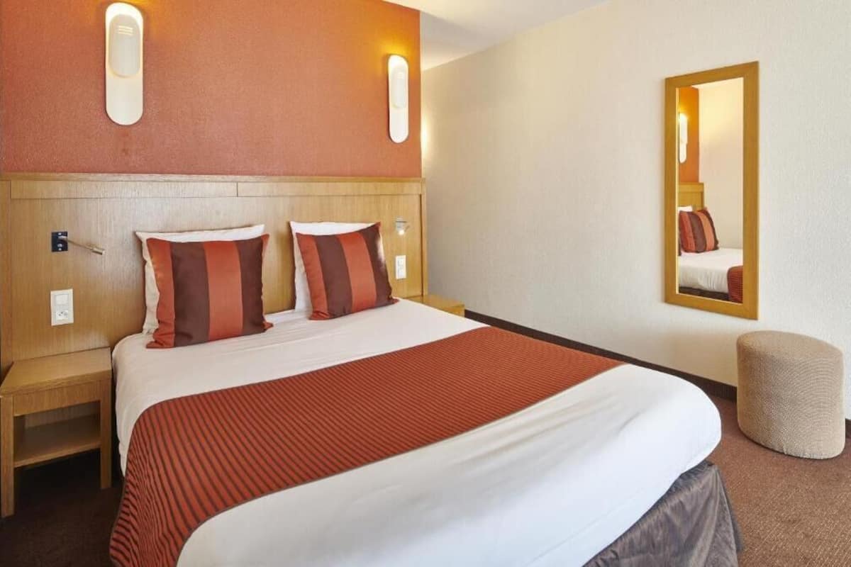 A hotel room with a large bed, two bedside tables, a mirror, and a small ottoman.