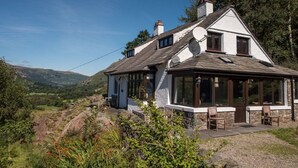 Une maison à deux étages, dotée d’un toit en pente, de grandes fenêtres et de fondations en pierre.