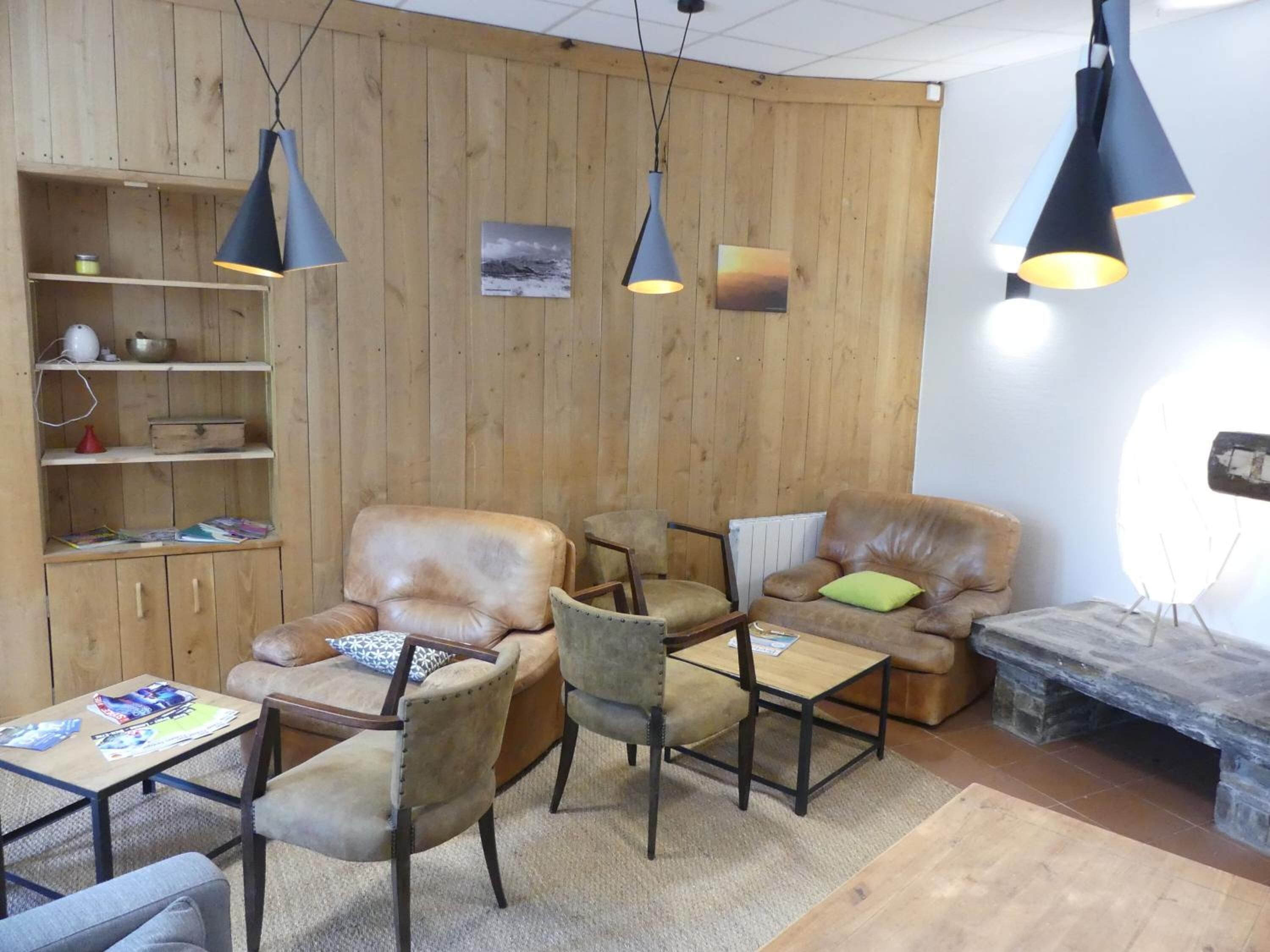Una sala de estar acogedora con paredes de madera, sofás de cuero y una chimenea de piedra. Dos lámparas colgantes iluminan el techo.