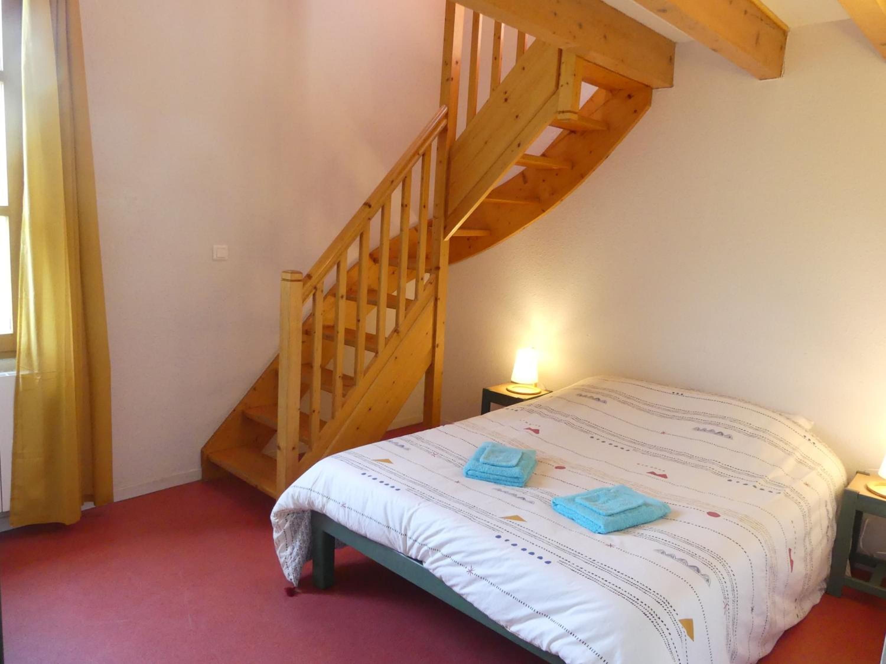 Un dormitorio con una escalera de madera, una cama con colcha a rayas y dos lámparas de noche.
