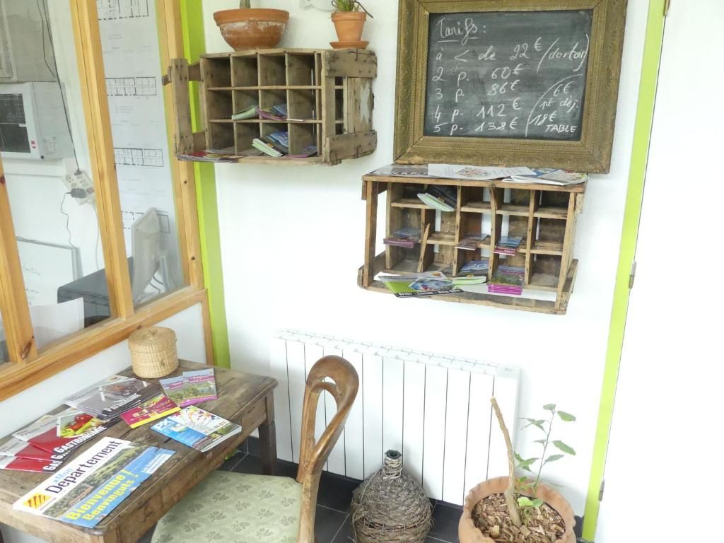 Una habitación con una mesa de madera que muestra libros y revistas, una ventana con persianas, un radiador y un menú de pizarrones con precios.
