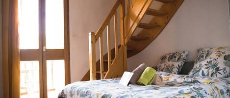Un dormitorio con techo inclinado, escalera de madera, cama con ropa de cama floral y ventana con cortinas.
