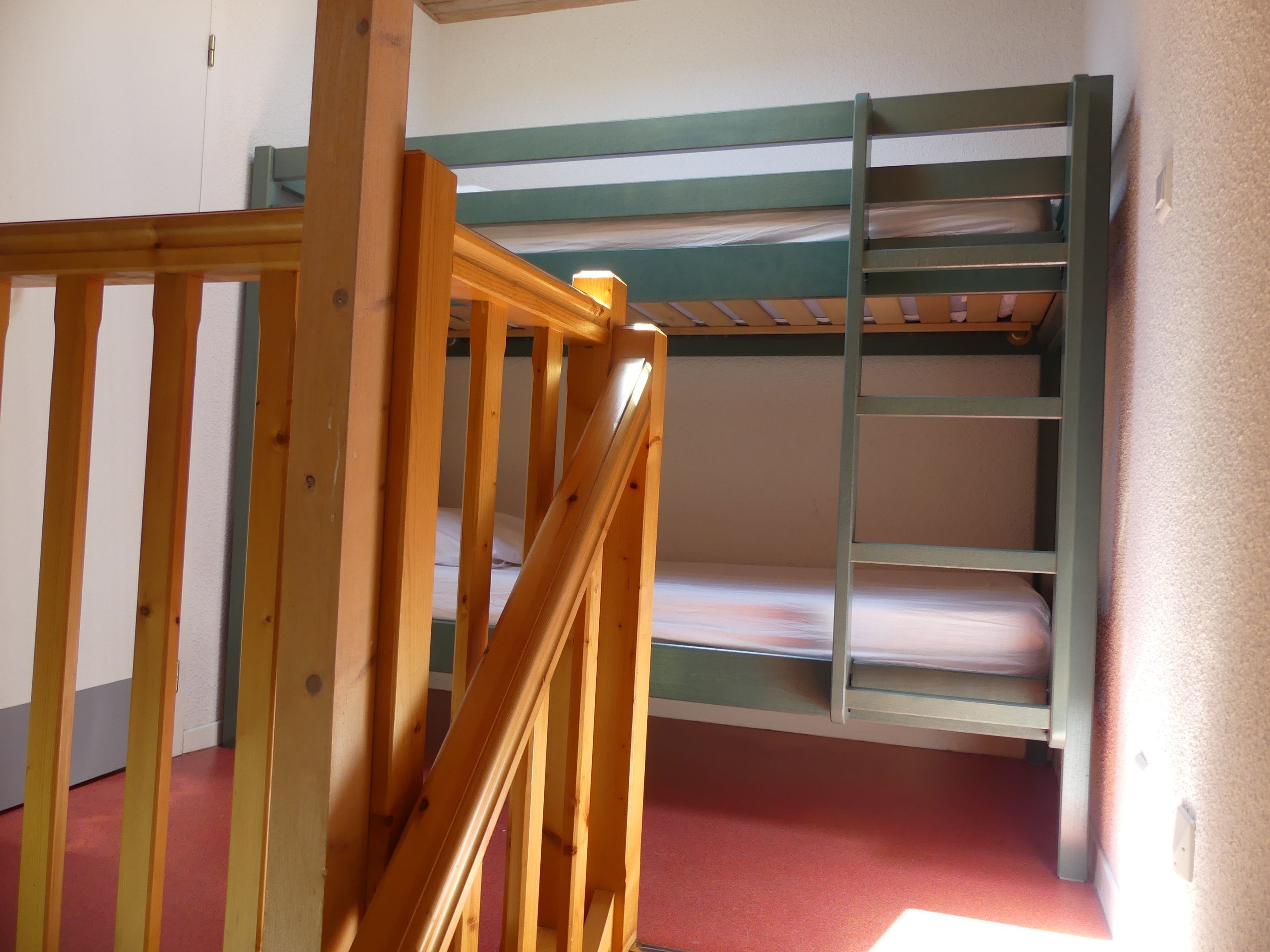 Una litera con escalera de madera y una cama inferior con colchón.
