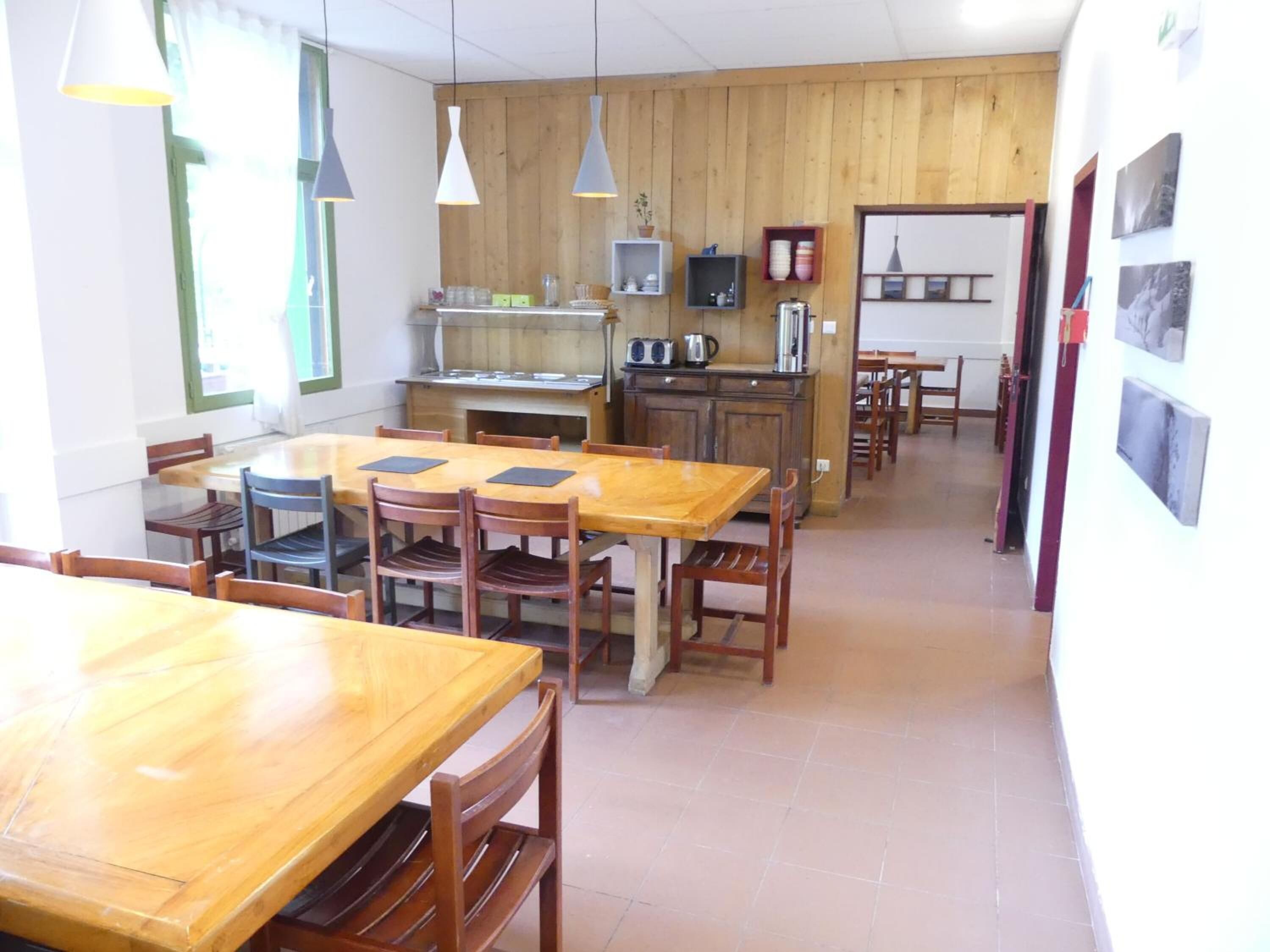 Een eetruimte met houten tafels en stoelen, een keuken met houten kasten, en hanglampen.
