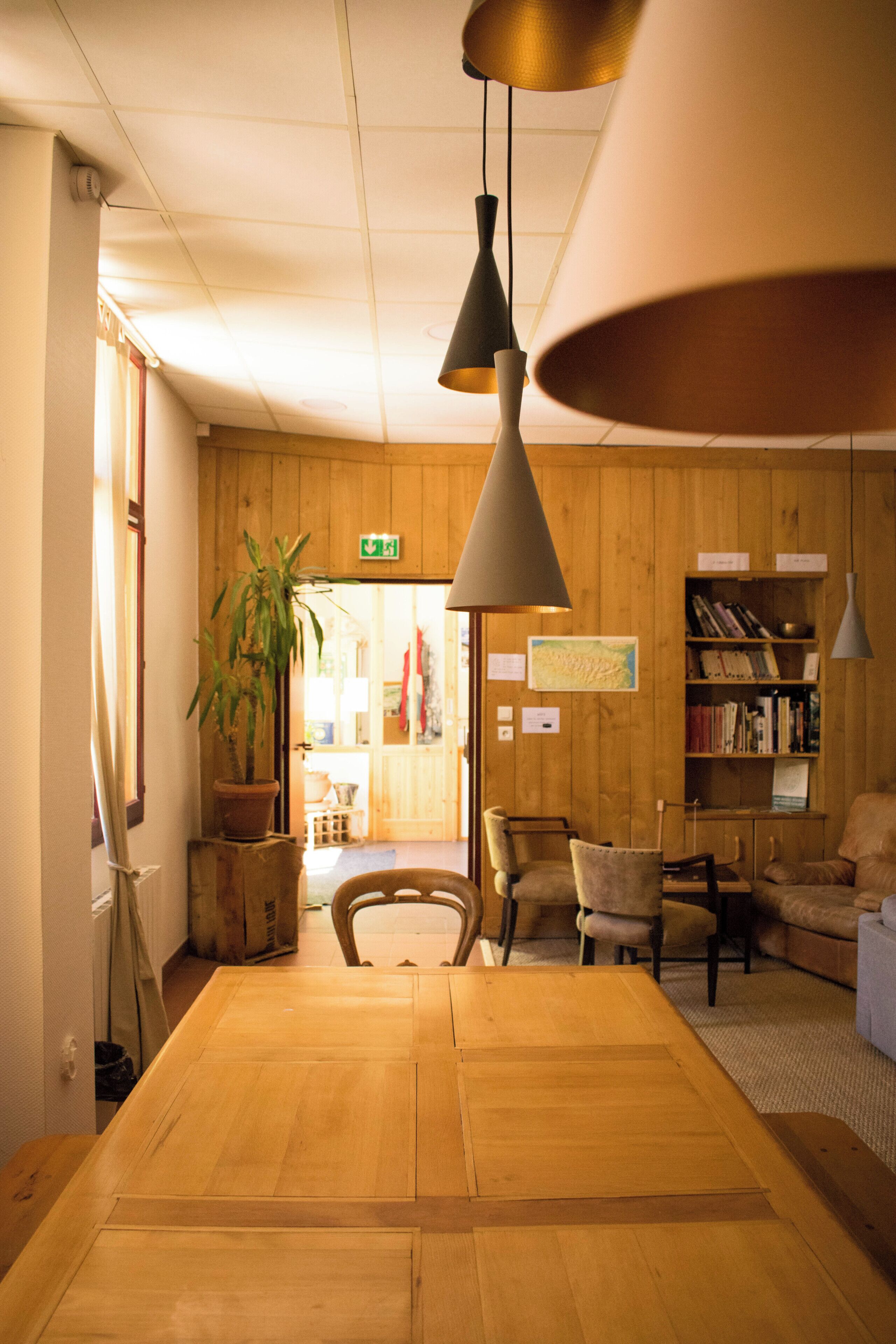 Un intérieur en bois comprenant une table à manger, des chaises, une bibliothèque et des lampes suspendues.