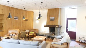 A cozy living room with wooden walls, a stone fireplace, leather sofas, and pendant lighting. - Gite de Llo (Llo)