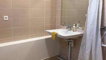 Un baño con bañera, lavamanos con espejo y cortina de ducha.