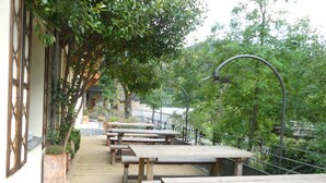 An outdoor seating area with wooden tables and benches, surrounded by greenery and a railing. - Gite de Llo (Llo)
