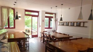 A dining area with multiple wooden tables and chairs, large windows with red frames, and hanging pendant lights. - Gite de Llo (Llo)