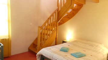 Un dormitorio con una escalera de madera, una cama con colcha a rayas y una lámpara de noche.